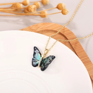Detail view of a golden butterfly pendant with dark iridescent resin and sparkling crystals