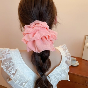 Detail view of a pink pleated ruffled scrunchie on a braided hairstyle with soft lighting