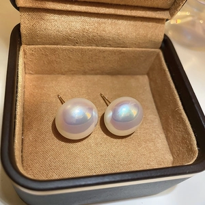 Macro view of white pearl stud earrings with iridescent luster in a brown velvet box