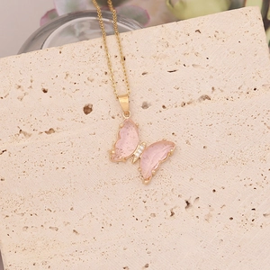 Détail d'un collier doré avec un pendentif papillon rose translucide et zircon blanc