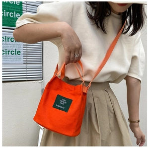 Detail of bright orange canvas bucket bag featuring a minimalist woven text label