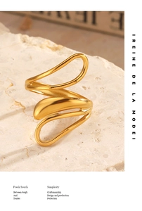 Detailed view of a gold wavy open ring on a textured beige stone background