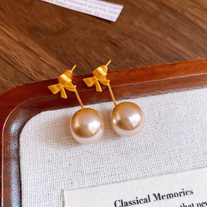Detail of elegant gold bow earrings with pearls on a textured display card