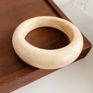 Macro shot of a cream marbled resin wide bangle displayed on a rustic wood stand