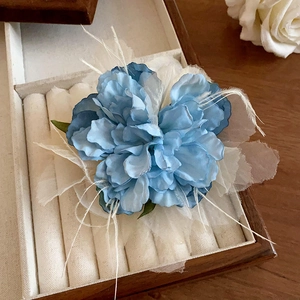 Detail of blue fabric rose hair clip with white feathers in a wooden jewelry box