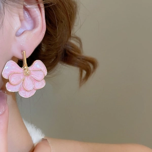 Close-up of elegant pink flower earrings with gold edges worn by a female model