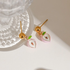 Macro shot of peach-shaped enamel earrings with golden metal base and delicate details