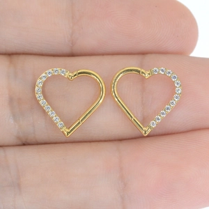 Detailed macro view of gold heart-shaped hoop earrings with clear cubic zirconia on fingertips