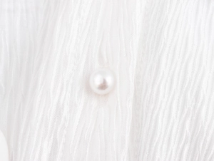 Close-up of white textured fabric with a round faux pearl button on the shirt