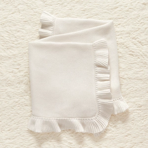 Close-up of white knitted baby blanket with ruffle edges on soft plush background