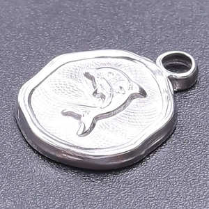 Macro shot of silver stainless steel pendant with embossed dolphin design on dark surface