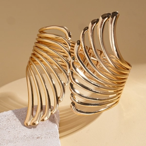 Detail of a golden cutout wing cuff bracelet on a minimalist textured stone background