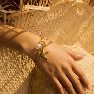 Close-up of golden stainless steel bracelet with starfish and seashell charms on wrist