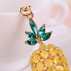 Close-up of golden pineapple pendant with green rhinestones and cat eye stones