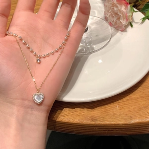 Double-layered gold necklace featuring a pearl strand and a mother-of-pearl heart pendant