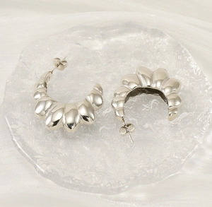 Detailed macro view of silver stainless steel C-shaped croissant earrings on glass