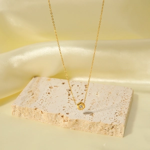 Minimalist gold necklace with a hexagonal zircon pendant on a luxury beige silk backdrop