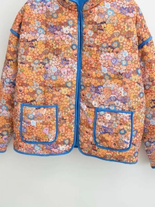 Detail of floral quilted jacket featuring blue contrast piping and dual patch pockets