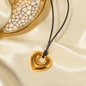 Collier cœur ajouré doré minimaliste avec cordon noir sur fond de soie blanche élégante