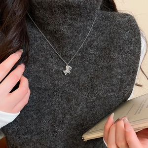 Detail of silver chain necklace with abstract pendant worn over a dark grey turtleneck