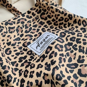 Detail of leopard print canvas tote bag featuring a stitched brand label and premium texture