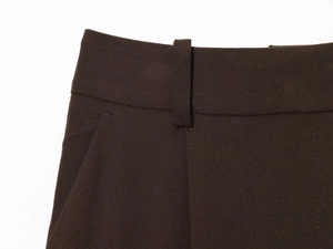 Detailed close-up of dark brown woven trouser waistline with belt loops and clean stitching