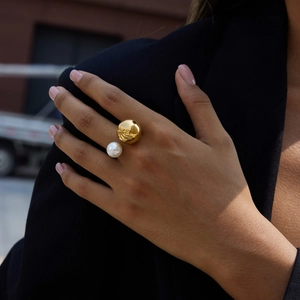 Close-up of minimalist gold ring with pearl on model hand against urban background