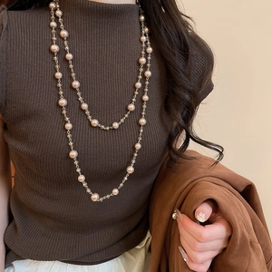 Detail view of a double-layered pearl and glass bead sweater necklace on a brown knit top
