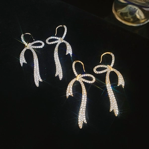 Sparkling zircon bow fringe earrings in gold and silver finish on black velvet background