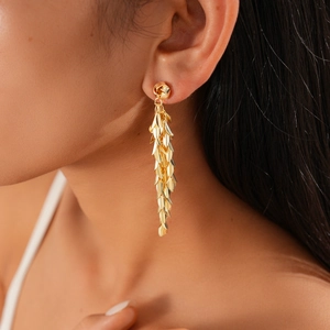 Macro detail of gold-plated leaf tassel earrings on model showing flowing metal fringe