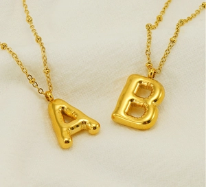 Golden 3D bubble style alphabet pendants A and B on ball chains over a beige background