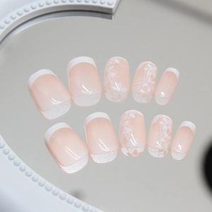 Short French tip press-on nails with white floral art and nude pink base on a mirror