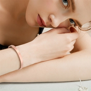 Primer plano de un brazalete minimalista en forma de C de oro rosa mate en la muñeca de un modelo.