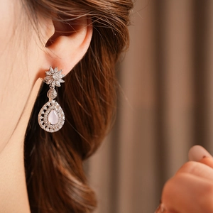 Close-up of sparkling floral drop earrings with pink pear-cut zircon on model ear