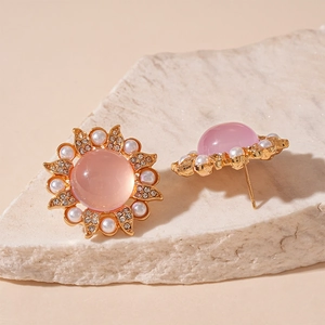 Macro shot of pink resin flower earrings with white pearls on a white stone surface