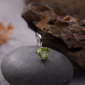 Macro shot of heart-shaped green gemstone pendant on silver base over dark pebble