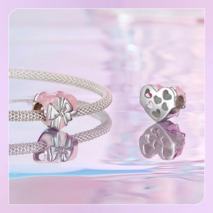 Macro detail of a 925 silver heart charm with pink enamel and a silver bow on a bracelet
