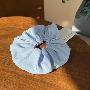 Close-up of light blue fabric scrunchie with button detail and tag on a wood table