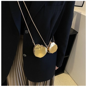 Detail of heart-shaped gold mini chain bag styled on a blazer and pleated skirt