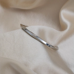 Close-up of minimalist twisted silver cuff bracelet on smooth champagne silk fabric