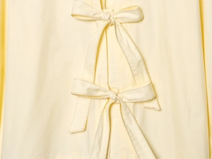 Detailed close-up of light yellow poplin shirt featuring two delicate front bow ties