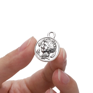 Silver alloy coin pendant with vintage profile relief held by fingers against white background