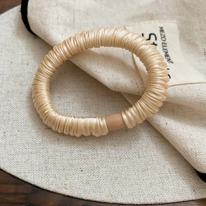 Close-up of champagne pleated elastic hair tie showing ribbed texture and seamless join