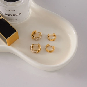 Détail de boucles d'oreilles créoles dorées avec strass larges et fines sur plateau
