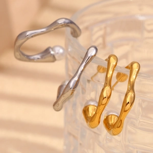Macro detail of gold and silver irregular C-shape earrings with pearls on glass