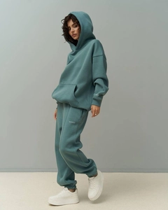 Close-up of WS STUDIO CO branding on oversized sage grey hoodie and jogger set