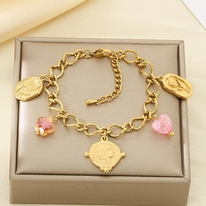 Detailed view of a gold chain bracelet with coin, heart, and flower charms on silk