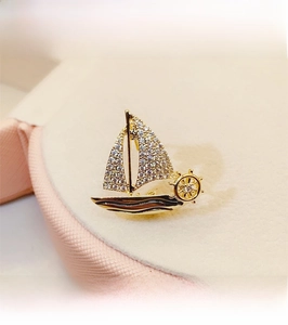 Macro shot of gold-plated sailboat brooch with crystal inlay and nautical helm detail