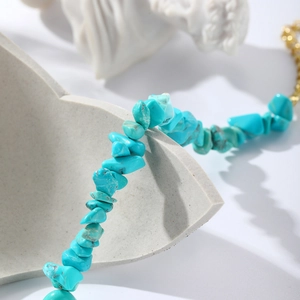 Detail of bohemian turquoise stone bracelet with gold chain on grey geometric stand