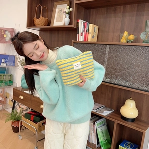Detail of yellow and blue striped plush cosmetic bag held by a model in a cozy setting